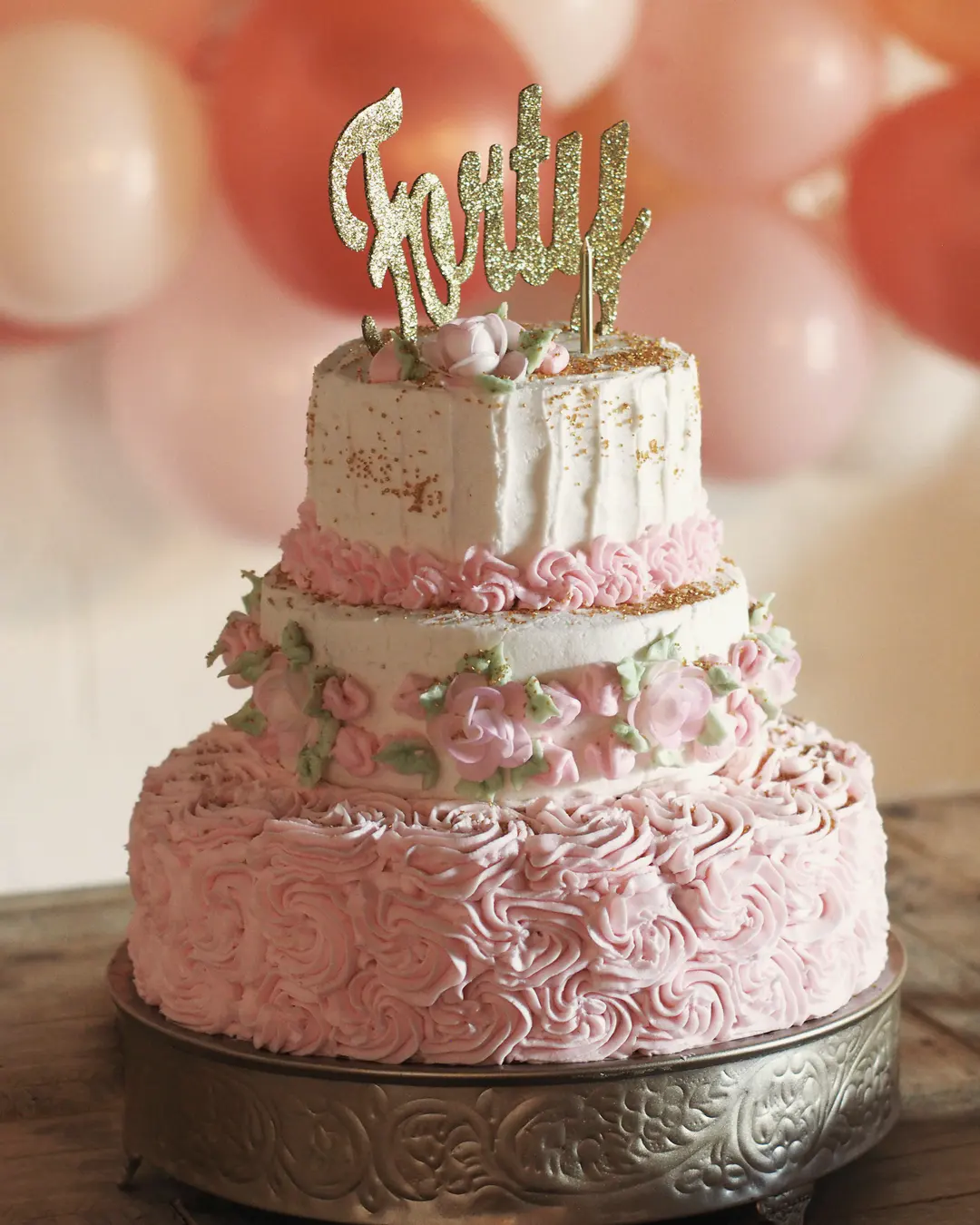 Stock photo: a three-tier pink and white birthday cake with buttercream rosettes and a gold “Forty” topper
