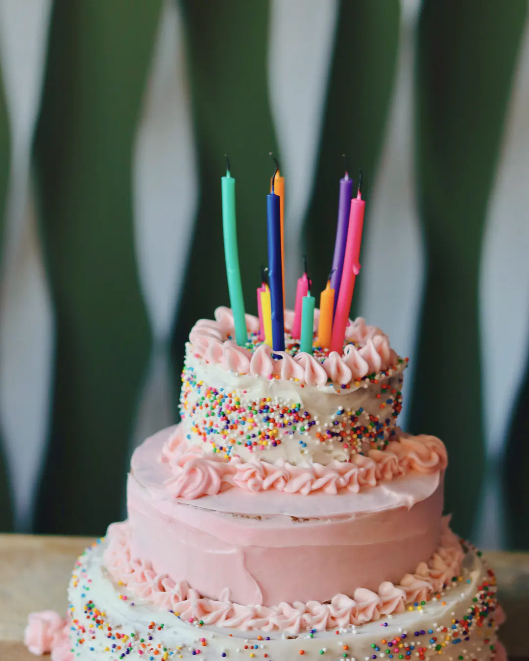 Stock photo: a tiered pink birthday cake covered in rainbow sprinkles with tall colorful candles