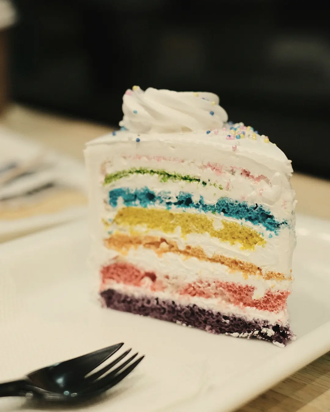 Stock photo: a slice of rainbow layer cake with white frosting on a plate with a fork