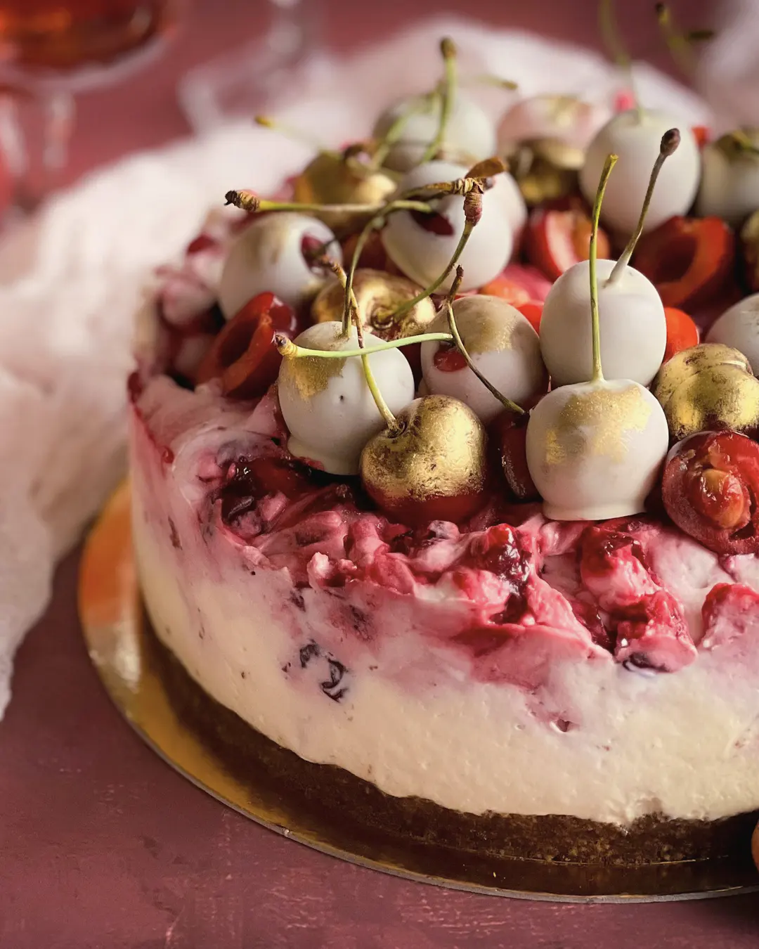Stock photo: a cake crowned with fresh cherries, some dipped in white and gold, on a wine-red background