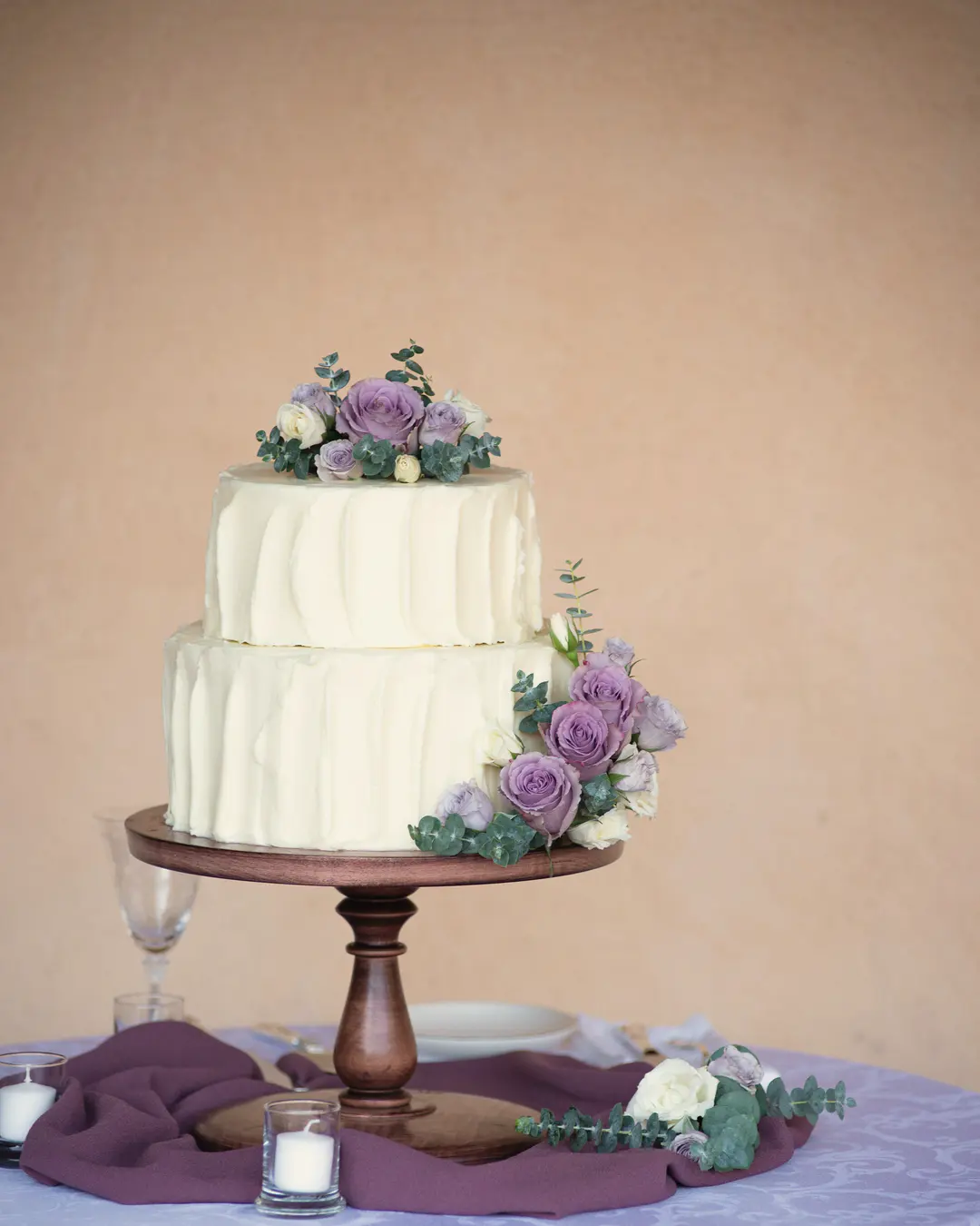 Stock photo: a white two-tier cake with purple roses on a wooden pedestal stand