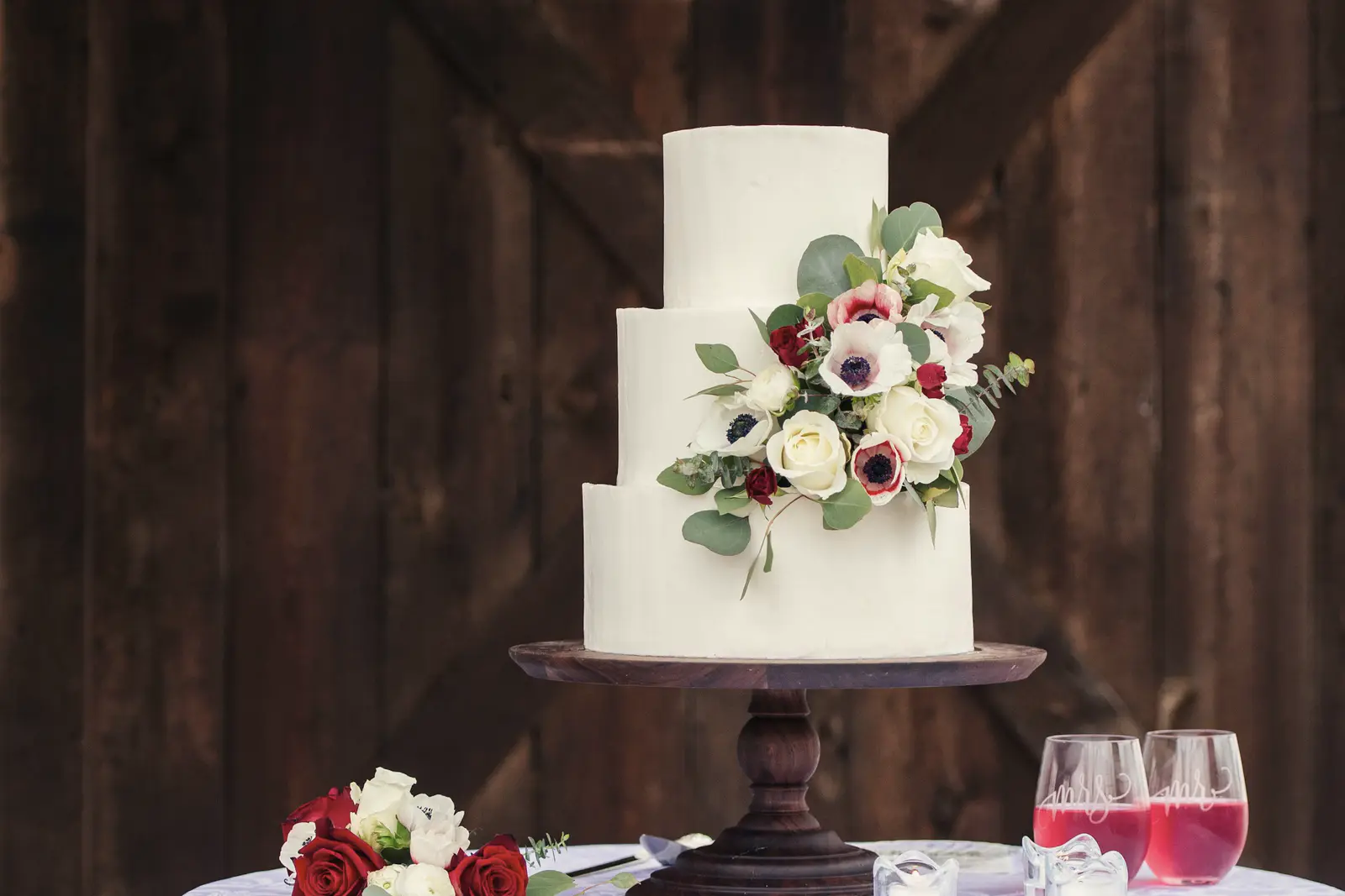 Stock photo: a three-tier white cake with roses, white blooms and greenery on a dark wooden stand