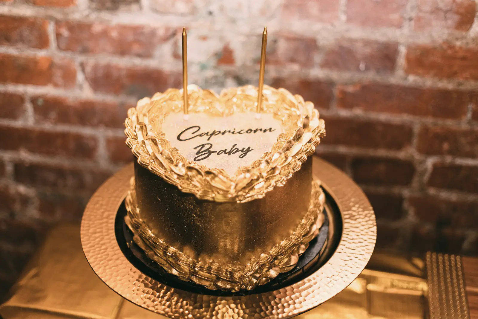 Stock photo: a gold vintage-style heart cake with ruffled piped borders and the message “Capricorn Baby”, on a hammered gold cake board